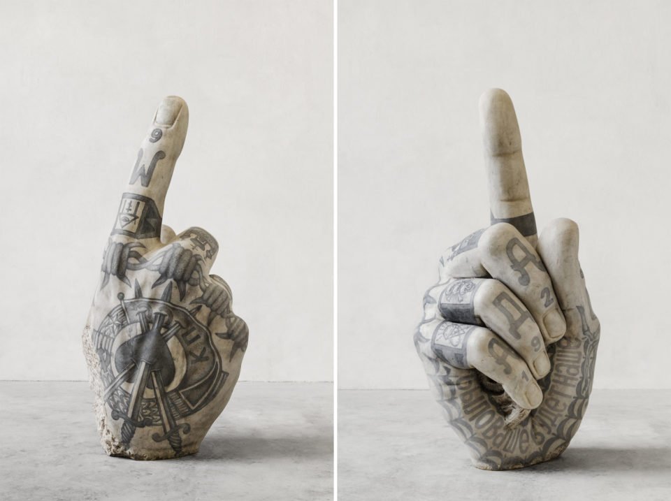 Duas fotos de esculturas de mãos mostrando totalmente tatuadas com artes genéricas