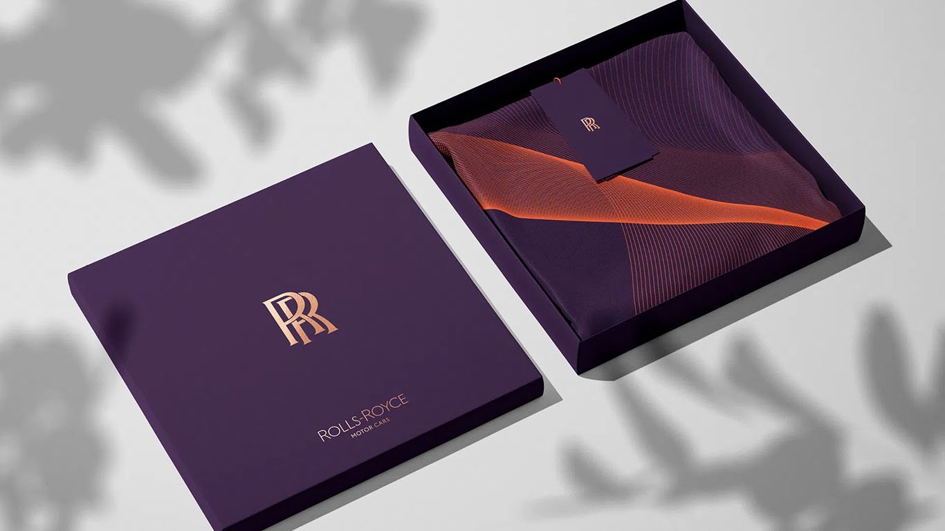 Caixa cor vinho da Rolls Royce, com o monograma dourado da marca na capa e Spirit of Ecstasy em linhas 3D no interior